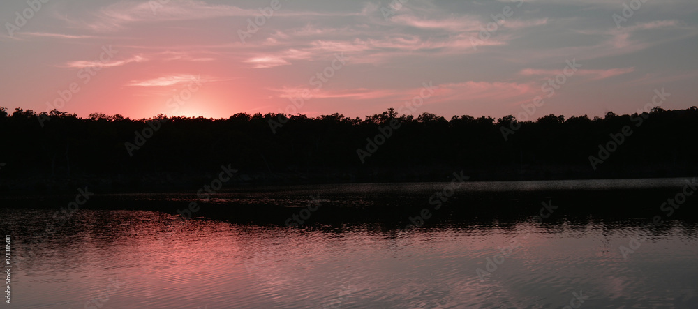 Naklejka premium Lake Sunset/PInk sunset reflection over a lake and trees.
