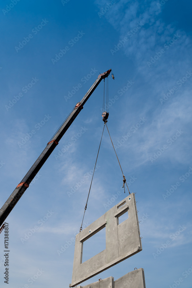 Construction site crane is lifting a precast concrete wall panel. Construction site crane is lifting a precast concrete wall panel.