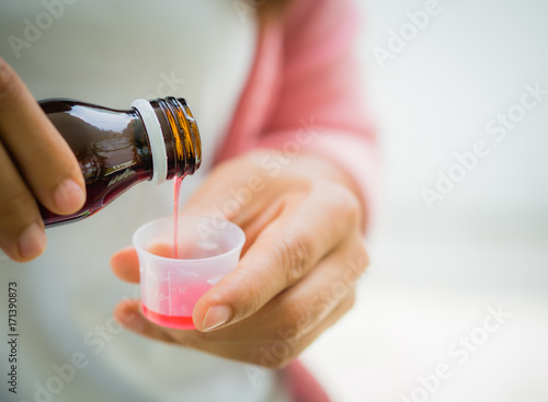Closeup woman pouring medication or antipyretic syrup from bottle to cup. Healthcare, people and medicine concept - photo