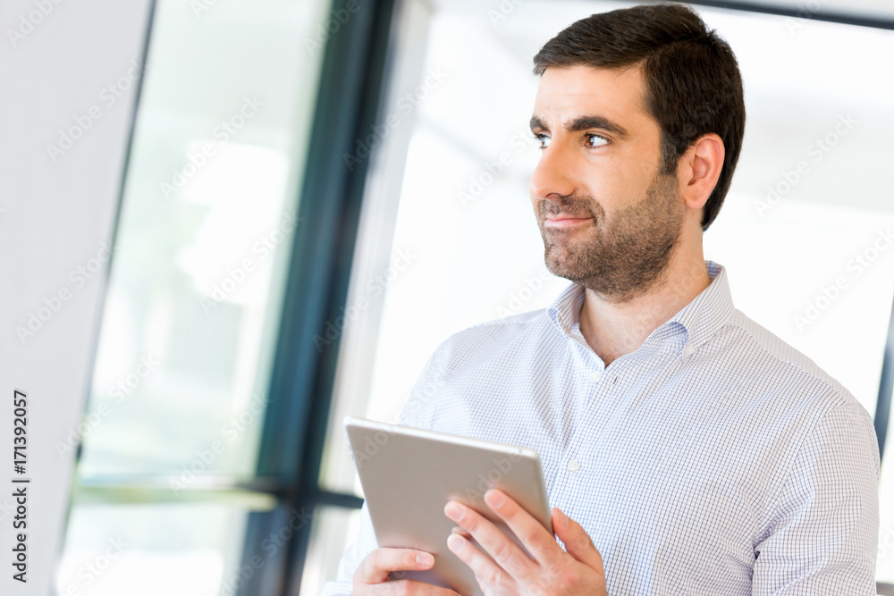 Young handsome businessman using his touchpad standing in office Young handsome businessman using his touchpad standing in office