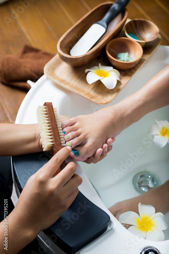 Obraz na plátně Manicure and pedicure series: Pedicurist brushing customer's foot in pedicure bo