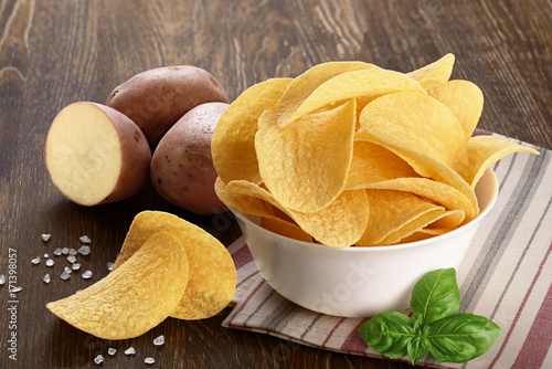 Potato and bowl with potato chips on a wooden background