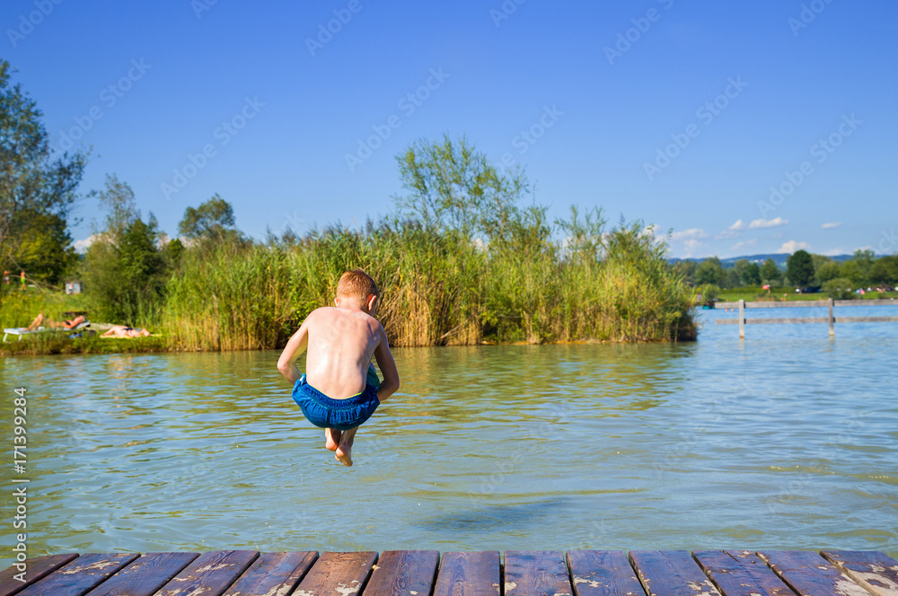Young happy boy is jumping into a lake on a sunny and bright day in Austria