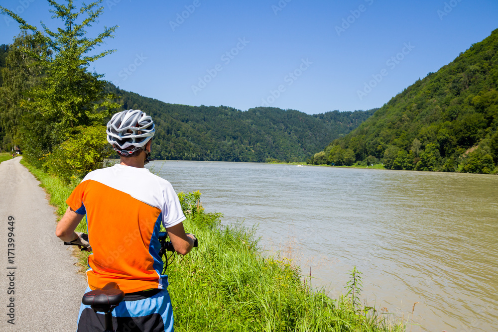 Fototapeta premium Young man is cycling on a sunny day along the Danube Cycle Route between Passau and Vienna