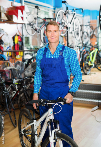 Positive male seller in uniform holding new bicycle