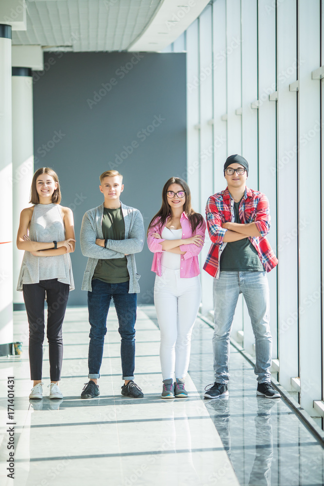 Four friends standing with crossed hands and smiling indoors. Fours students in university.