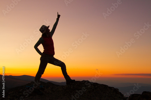 Sunset Silhouette of attractive woman staying and looking happy on top of the mountain. Freedom  adventure and leisure vacation concept.