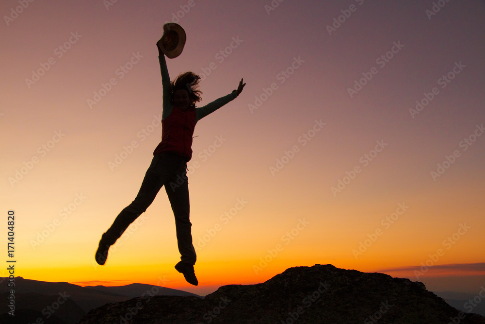 Silhouette of happy joyful young attractive woman jumping and having fun at the mountain against the sunset. Freedom, adventure and leisure vacation concept. Silhouette of happy joyful young attractive woman jumping and having fun at the mountain against the sunset. Freedom, adventure and leisure vacation concept.