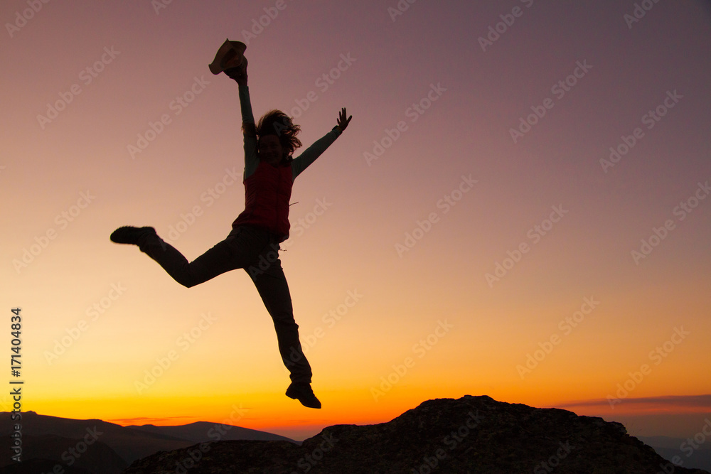 Silhouette of happy joyful young attractive woman jumping and having fun at the mountain against the sunset. Freedom, adventure and leisure vacation concept. Silhouette of happy joyful young attractive woman jumping and having fun at the mountain against the sunset. Freedom, adventure and leisure vacation concept.