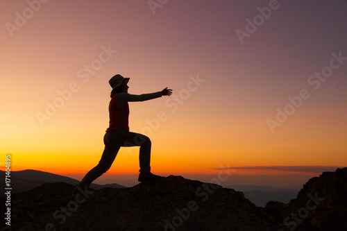 Silhouette of happy joyful young attractive woman jumping and having fun at the mountain against the sunset. Freedom  adventure and leisure vacation concept.
