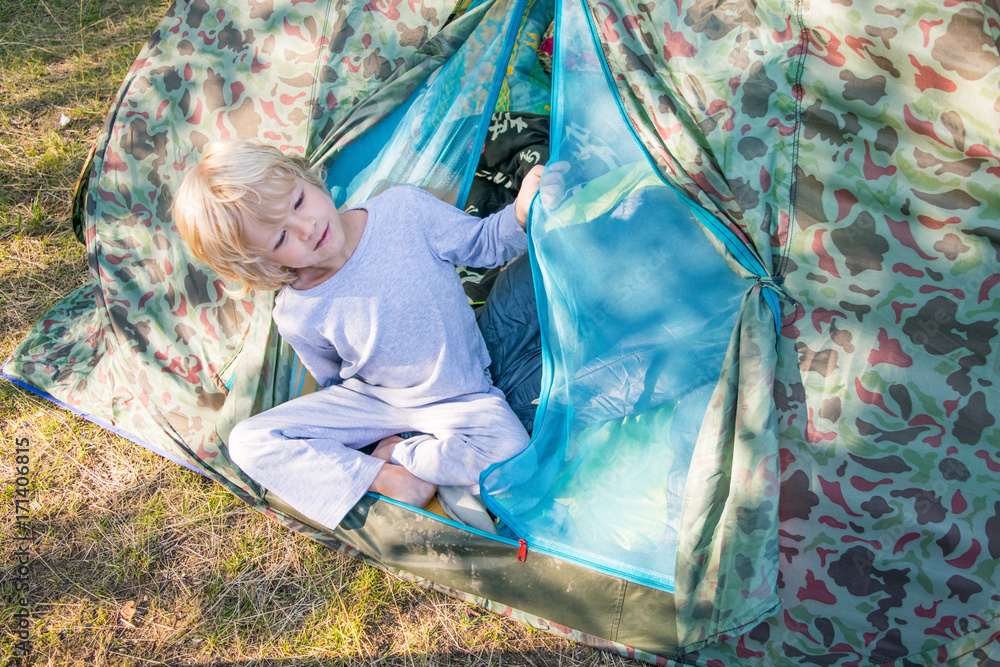Sleepy blond boy gets out a tent in a morning