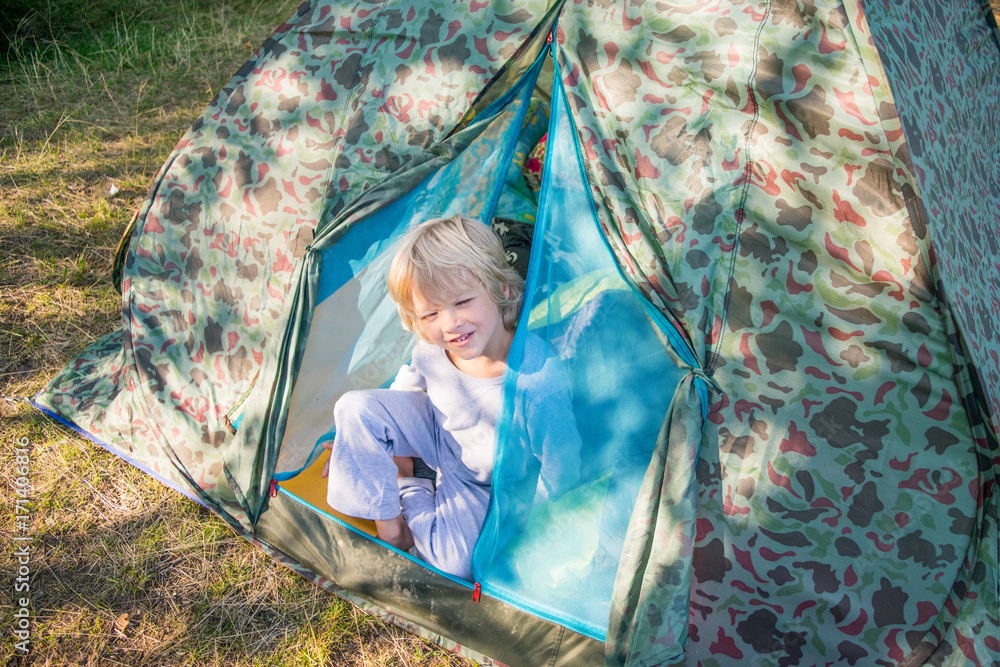 Sleepy blond boy gets out a tent in a morning