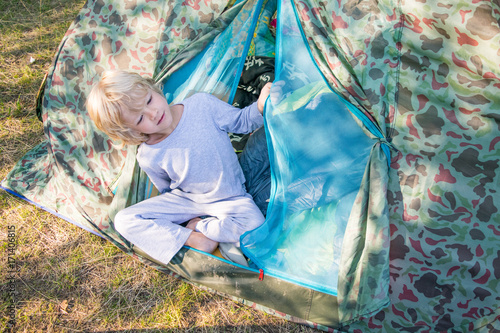 Sleepy blond boy gets out a tent in a morning