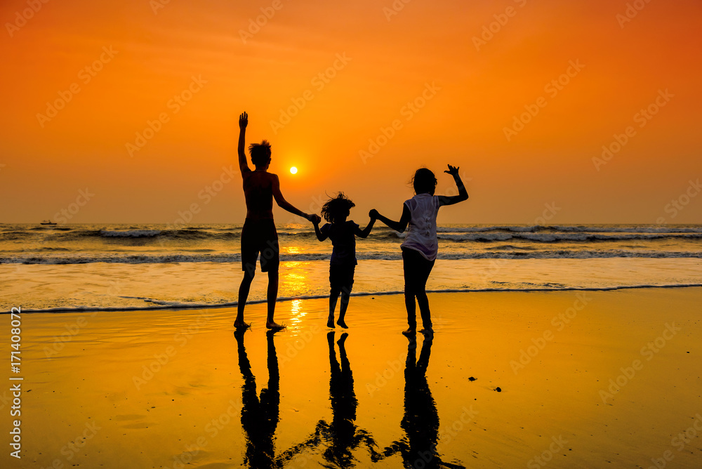 Silhouettes of group of happy children dancing on beach at sunset.