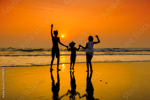 Obraz na płótnie Silhouettes of group of happy children dancing on beach at sunset. w salonie