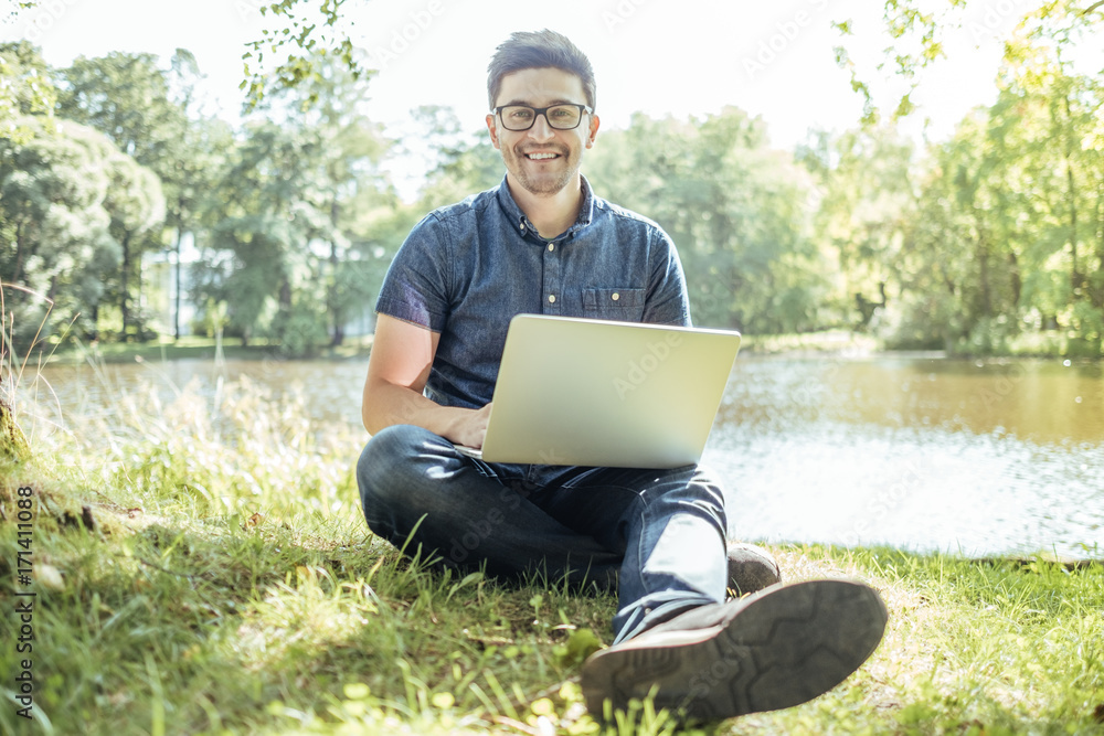 Young man with laptop outdoor sitting on the grass Young man with laptop outdoor sitting on the grass