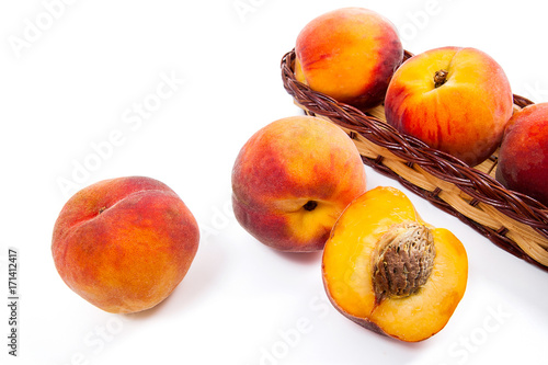 Whole and half of ripe peach fruit and several in basket isolated on white background.