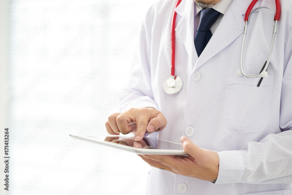 Unknown doctor posing usind digital table with bright background, he is wearing a stethoscope . Unknown doctor posing usind digital table with bright background, he is wearing a stethoscope .