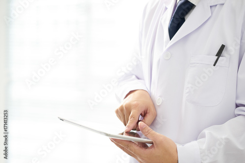 Unknown doctor posing usind digital table with bright background, he is wearing a stethoscope .