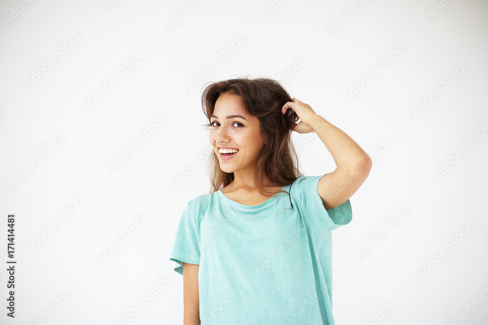 Isolated studio shot of charming pretty woman in casual t-shirt looking and smiling broadly at camera, having playful flirtatious expression on her cute face while posing against whte wall background Isolated studio shot of charming pretty woman in casual t-shirt looking and smiling broadly at camera, having playful flirtatious expression on her cute face while posing against whte wall background