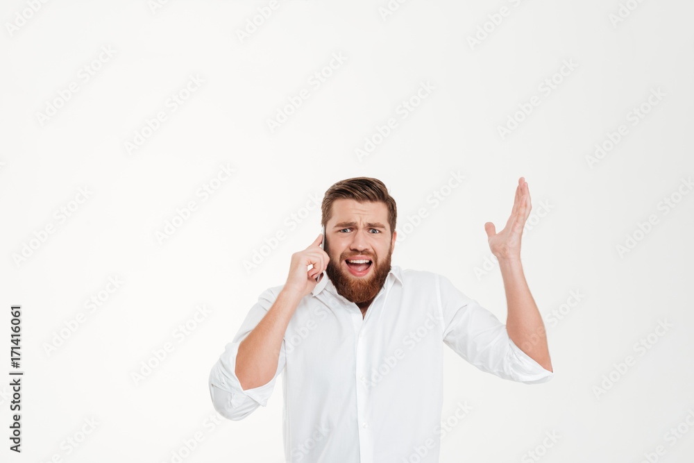 Angry young bearded emotional man talking by phone. Angry young bearded emotional man talking by phone.