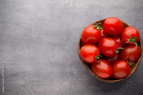Small plum tomatoes in a wooden bowl on a gray background.