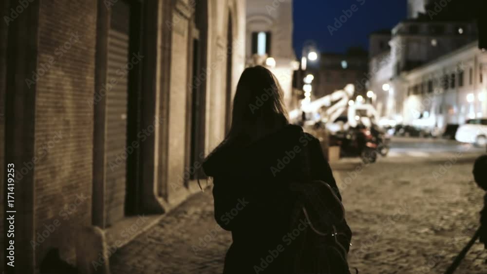 Back view of young stylish woman walking through the deserted lane late at night to main street, urban road. Back view of young stylish woman walking through the deserted lane late at night to main street, urban road.