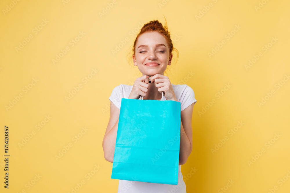 Fototapeta premium Pleased ginger woman holding packet in hands with closed eyes