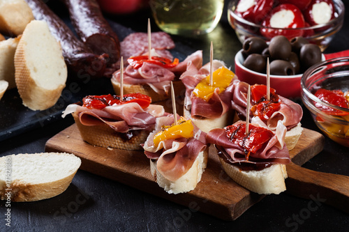 Spanish tapas with slices jamon serrano and grilled pepper. Also olives, salami, pickled onions, and peppers stuffed with cheese