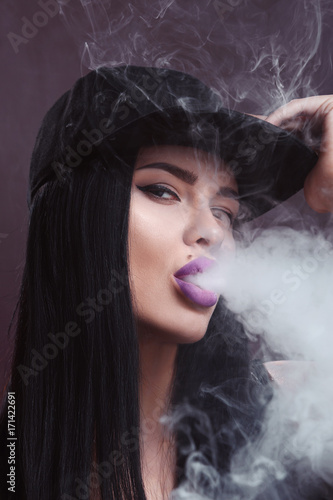 Young sexy woman is vaping. A cloud of vapor. Studio shooting.