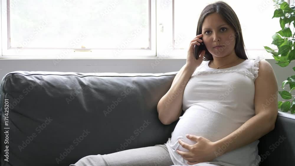 Pregnant woman with a mobile phone sits on a sofa at home. Pregnant woman with a mobile phone sits on a sofa at home.