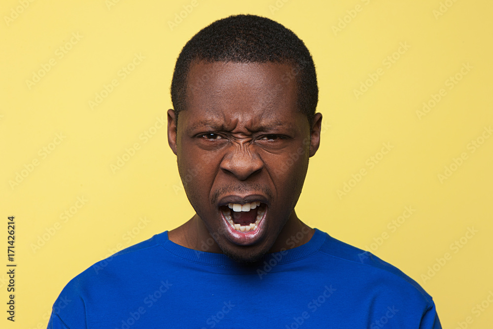 Angry screaming male. Rage emotion on pop yellow background. Evil African American man shouting, furious feelings, conflict concept Angry screaming male. Rage emotion on pop yellow background. Evil African American man shouting, furious feelings, conflict concept