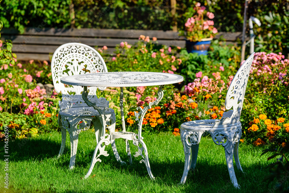 White metal outdoor furniture group in garden. One table and two chairs in  vintage style with autumn flowers in background. Stock Photo | Adobe Stock