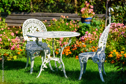White metal outdoor furniture group in garden. One table and two chairs in vintage style with autumn flowers in background.