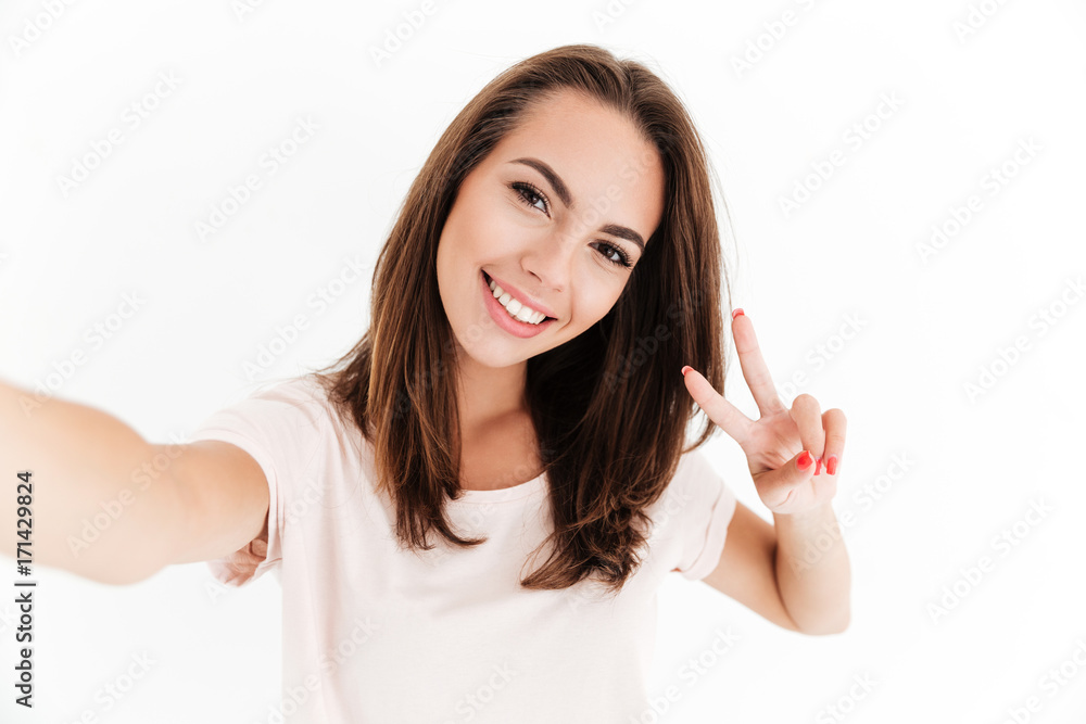 Pleased woman making selfie and showing peace sign at camera