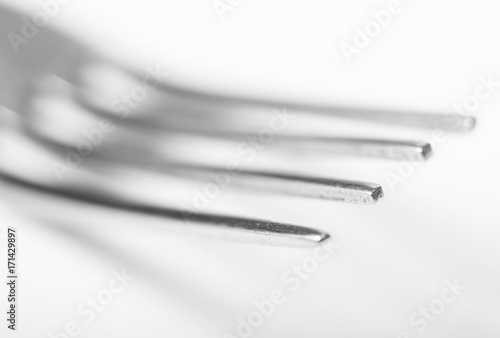 A close shot of the tines of a single silver fork on a white background showing regular wear and tear