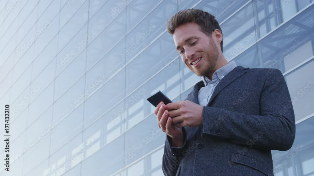 Businessman using phone sms texting using app on smartphone in city business district. Young business man using mobile phone smiling happy in suit jacket outdoors. Urban male professional. SLOW MOTION Businessman using phone sms texting using app on smartphone in city business district. Young business man using mobile phone smiling happy in suit jacket outdoors. Urban male professional. SLOW MOTION