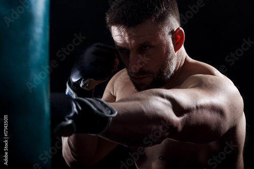 Studio shot of male boxer punching a boxing bag.