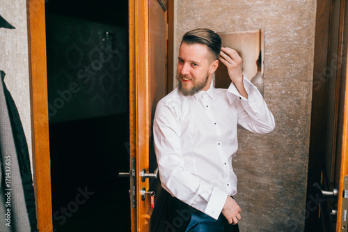 Handsome stylish groom with beard and mustache getting dressed and preparing for the wedding day.
