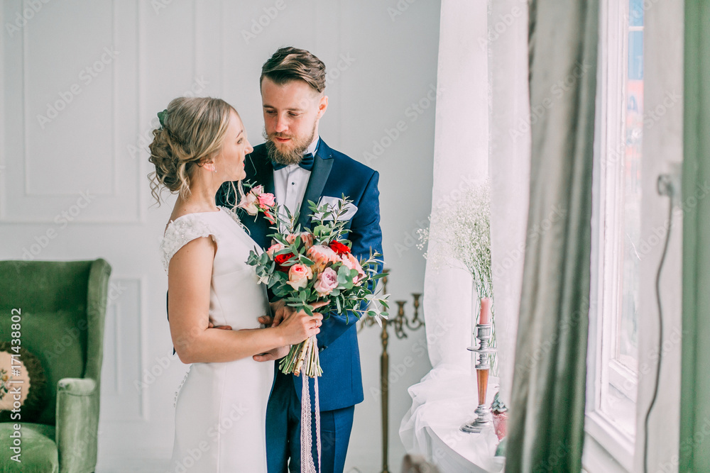 cute wedding couple in the interior of a classic studio decorated. they kiss and hug each other. Newkyweds looking. Bride and groom photoshoot