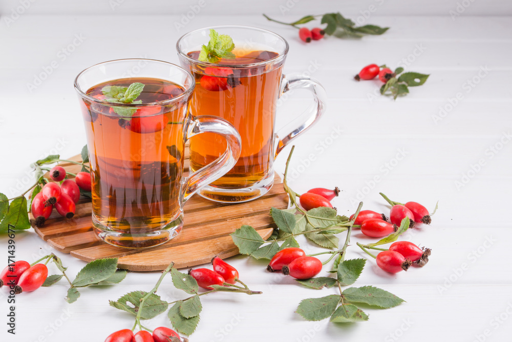 Rose hip tea in transparent cup with honey and fresh berries. Vitamin C drink on white background. Rose hip tea in transparent cup with honey and fresh berries. Vitamin C drink on white background.