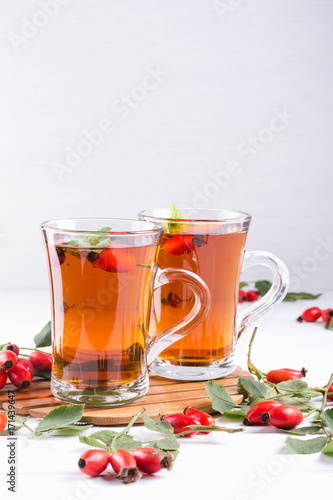 Rose hip tea in transparent cup with honey and fresh berries. Vitamin C drink on white background.