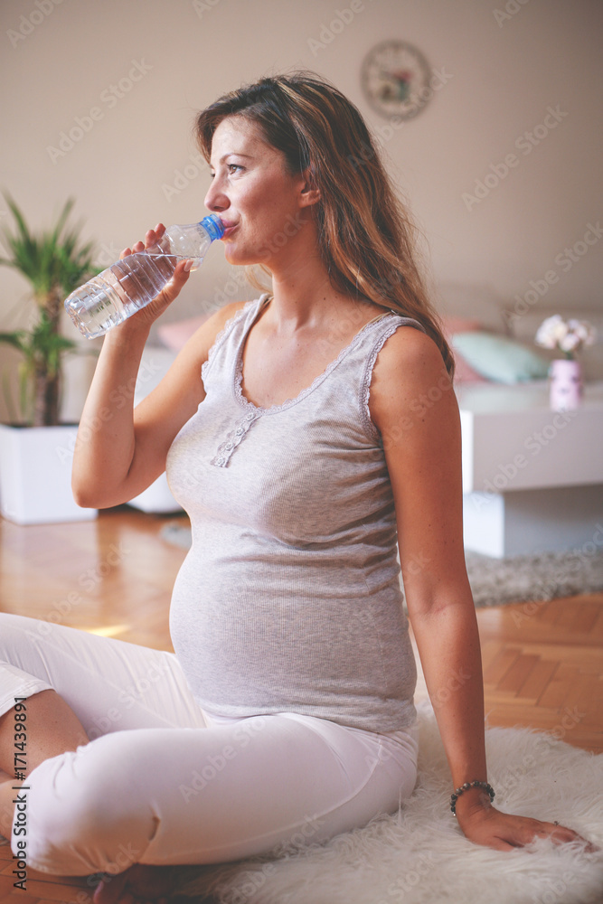Pregnant woman sitting on floor and drinking water. Pregnant woman sitting on floor and drinking water.