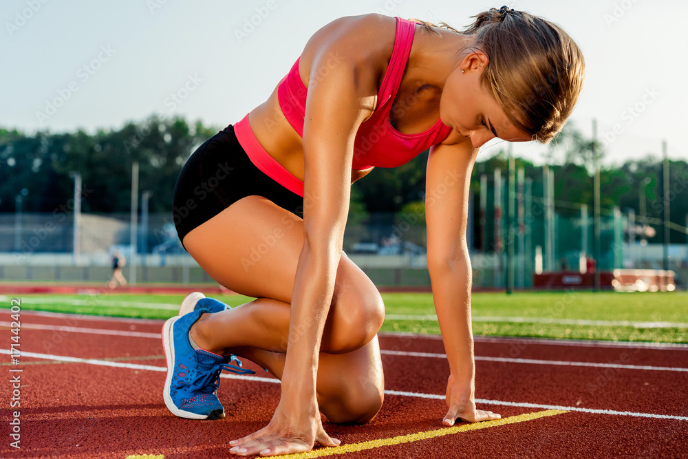 Young woman athlete at starting position ready to start a race on racetrack. Young woman athlete at starting position ready to start a race on racetrack.
