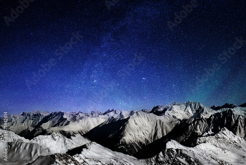 Mountains of the Alps at night, snowy peaks of a mountain range under a large starry sky