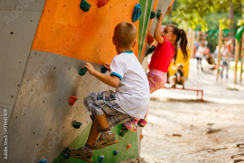Sporty children climbing artificial boulder on practical wall in gym