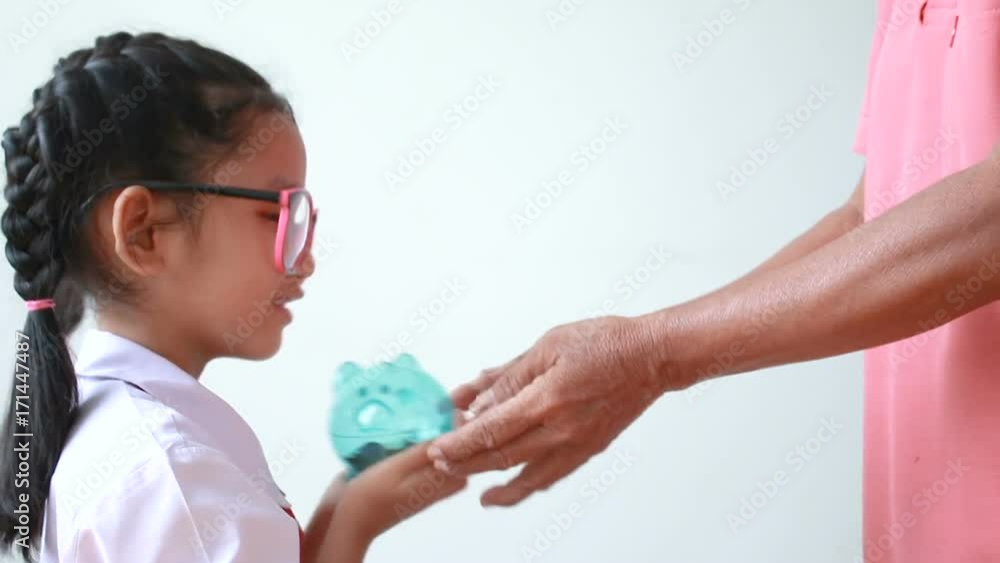 Hands of old woman grandmother giving clear piggy bank to Asian little girl over white background metaphor saving money for education concept Hands of old woman grandmother giving clear piggy bank to Asian little girl over white background metaphor saving money for education concept