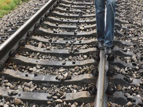 Man is walking on railroad track. Visible his feet.