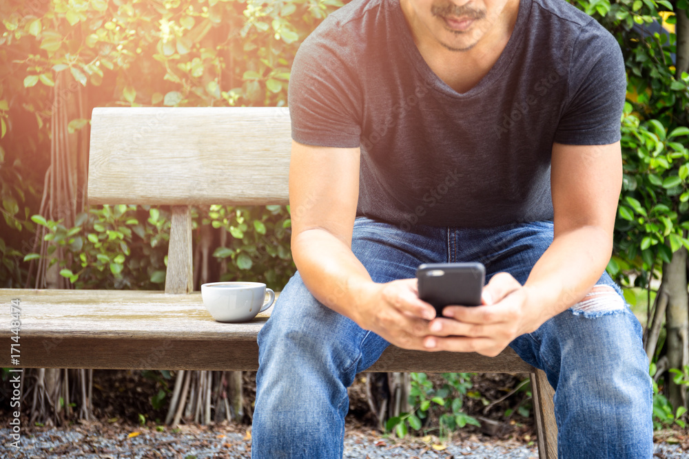 Man wearing ripped jean with cup of coffee using cell phone Man wearing ripped jean with cup of coffee using cell phone