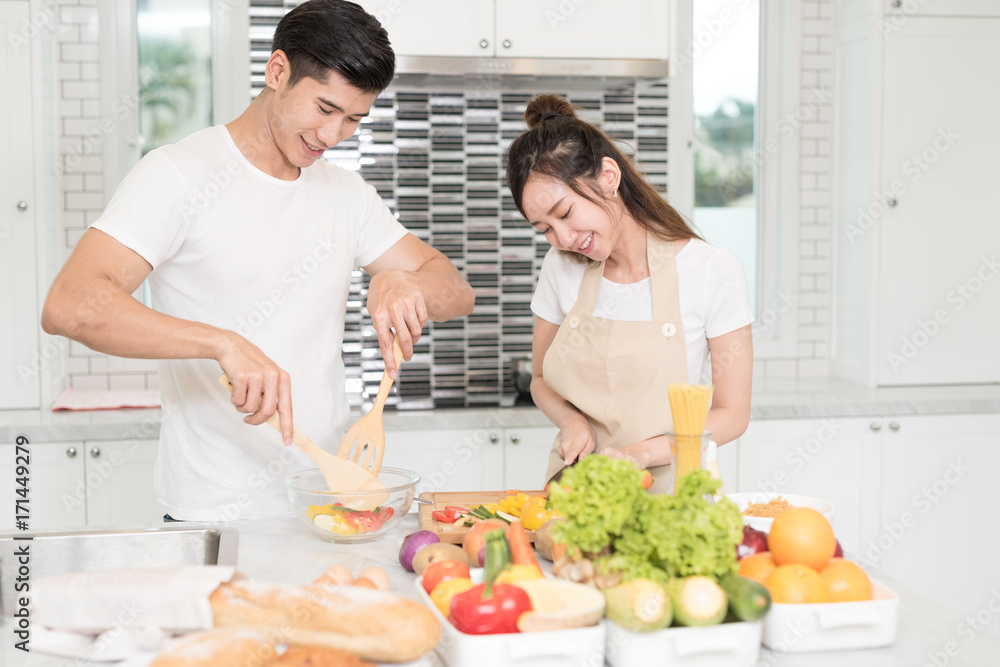 Happy young asian couple teasing and enjoy cooking together in the kitchen at home.